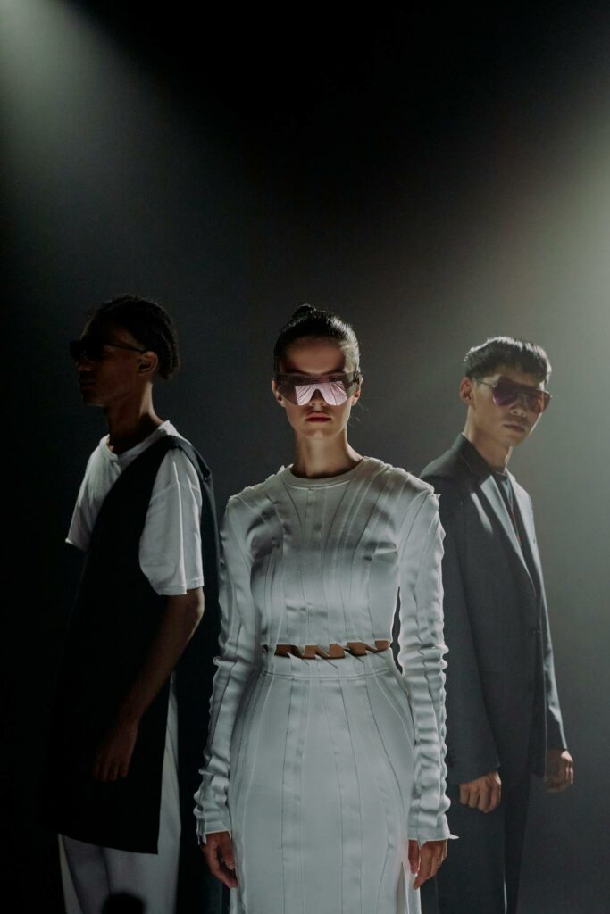 Dramatic studio shot of diverse models in stylish outfits and eyewear under moody lighting.