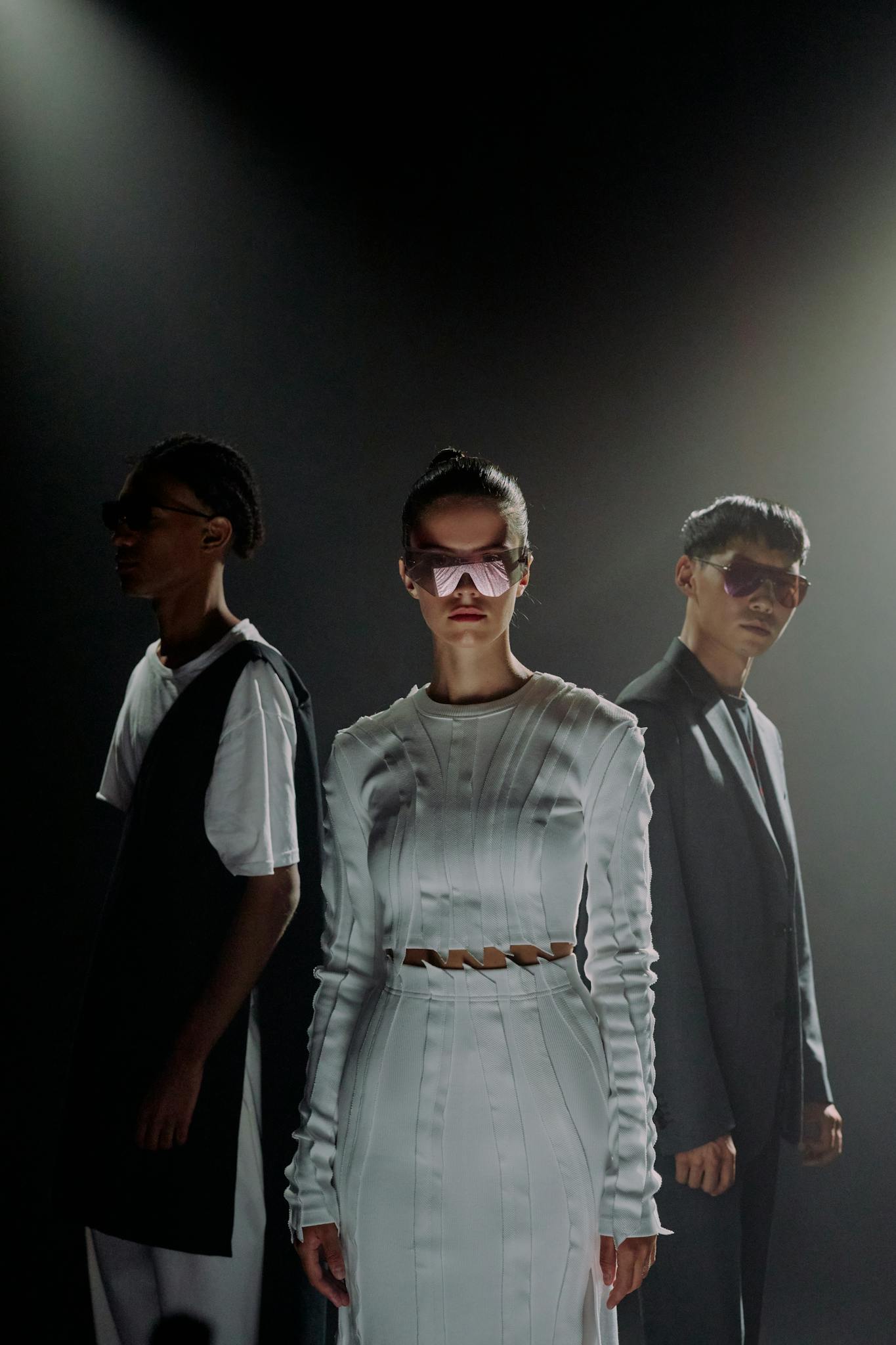 Dramatic studio shot of diverse models in stylish outfits and eyewear under moody lighting.