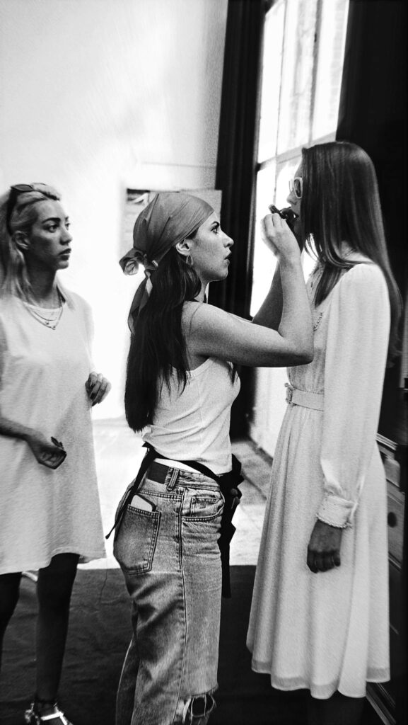 Three women engage in a fashion photoshoot makeup session.
